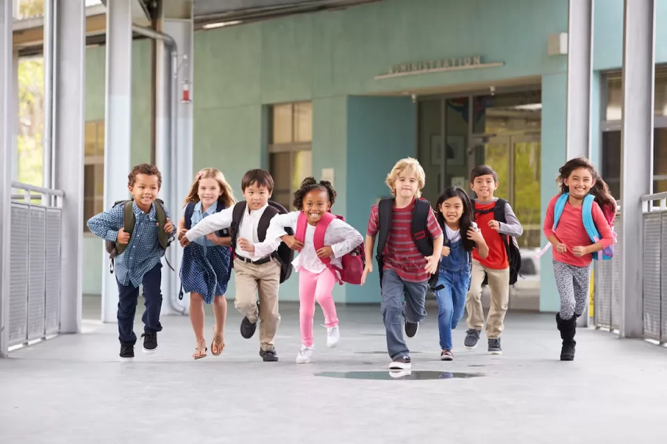 Group of elementary school children running in an outdoor corridor.